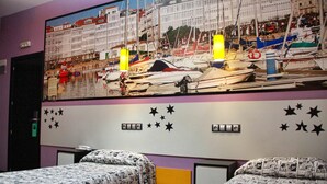 A hotel room with a large cityscape mural on the wall, two beds with patterned bedding, and a small desk with a lamp. - JC Rooms Santa Ana (Madrid)