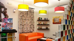 A room with an orange sofa, a coffee table, and a bookshelf filled with colorful glass bottles. - JC Rooms Santa Ana (Madrid)