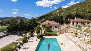 A pool area with stone buildings, a clear sky, and a mountainous backdrop. - Pleiades Studios - All Season Gems (Sikyona)