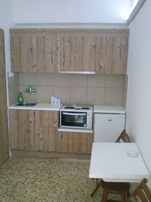 A compact kitchen with wooden cabinets, a microwave, a small refrigerator, and a tiled backsplash. - Villa Teo (Kalamata)