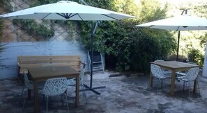 An outdoor patio with a wooden table and chairs, two white umbrellas, and a wooden bench. - Villa Teo (Kalamata)
