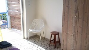 Um canto de um quarto com uma cadeira de plástico branca, um banquinho de madeira e uma porta de madeira.