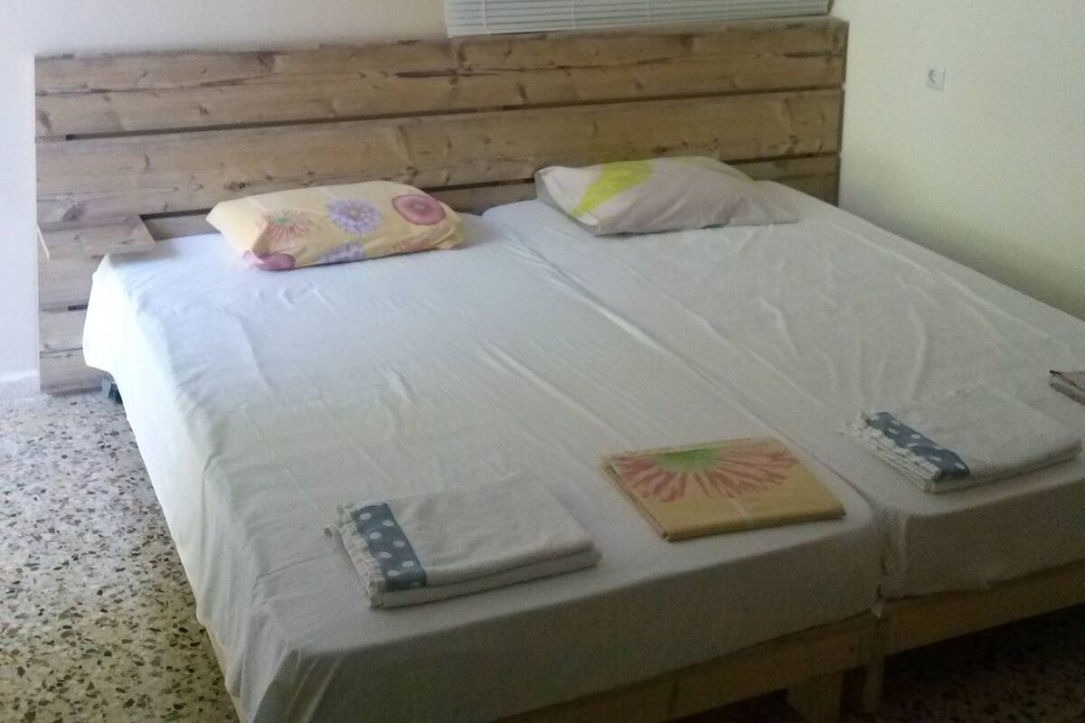 A bedroom with a wooden headboard, two beds with white linens, a window with blinds, and a ceiling fan.