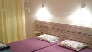 Quarto com cabeceira de madeira, duas camas com roupa de cama roxa e duas luzes fixadas na parede.