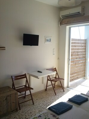 A room with a white desk, two wooden chairs, a television mounted on the wall, and a sliding door leading to an outdoor area. - Villa Teo (Kalamata)
