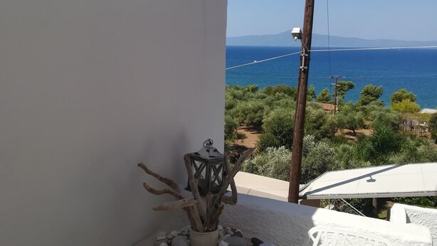 Uma varanda com vista para o mar, uma mesa pequena com uma planta decorativa e uma cadeira branca.