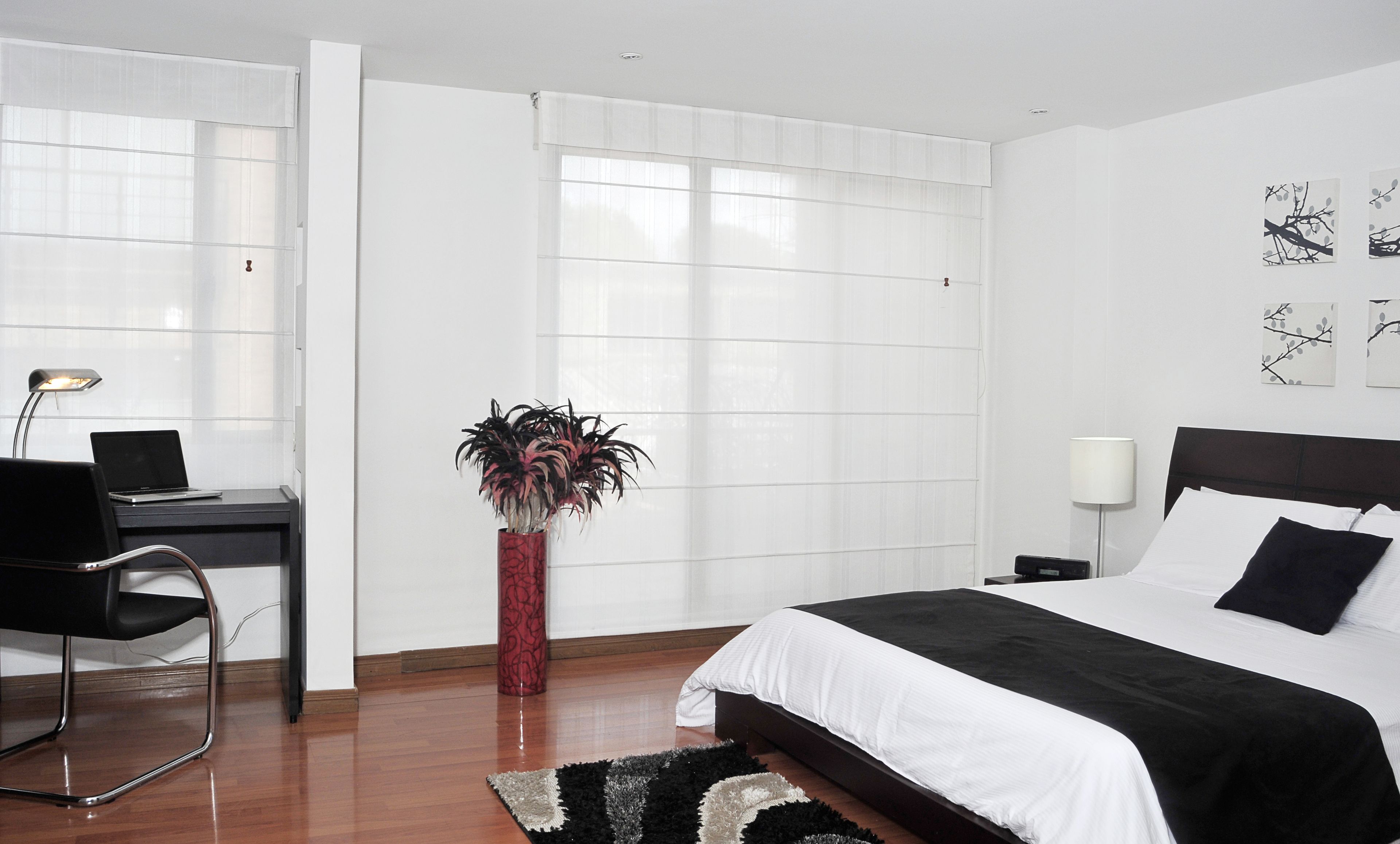 A modern hotel room with a bed, desk, chair, and a potted plant.