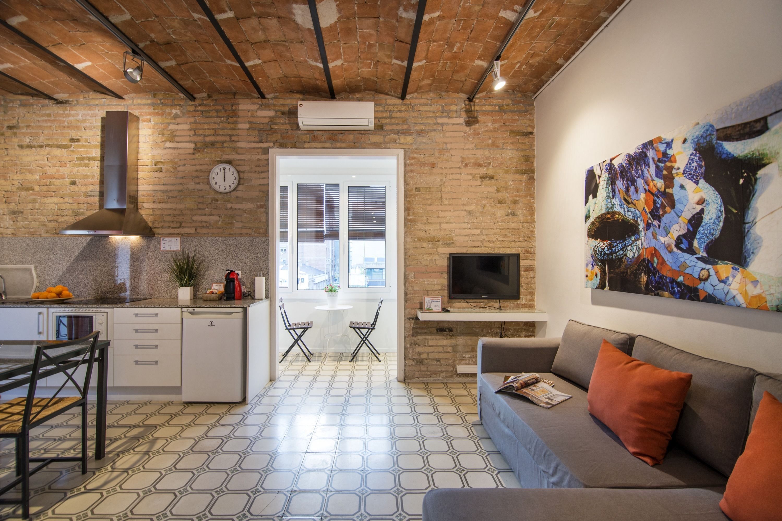 A modern kitchen with a dining area, a sofa, and a TV.