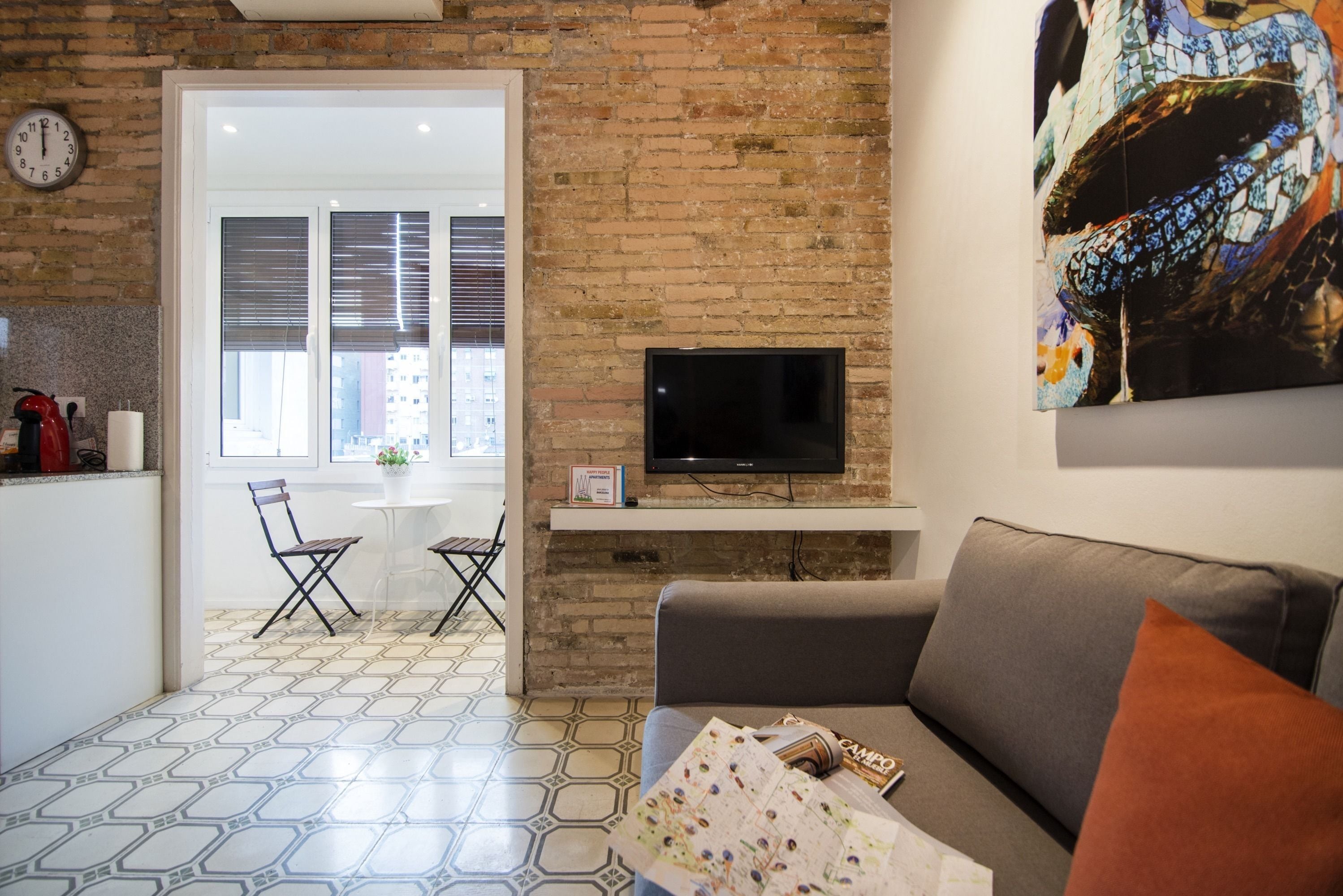 A living room with a brick wall, a flat-screen TV, a grey sofa, and a coffee table.