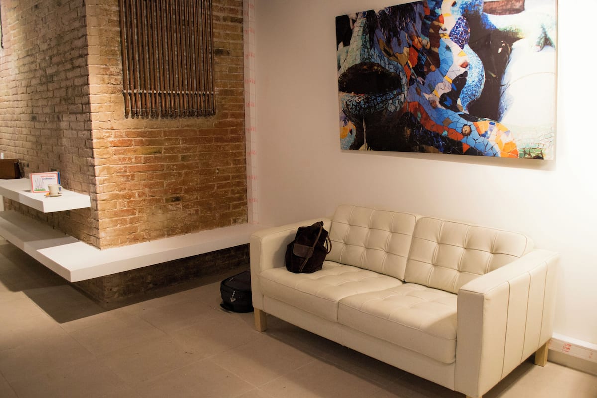 A room with a brick wall, a white sofa, a painting, and a small table with a sign.