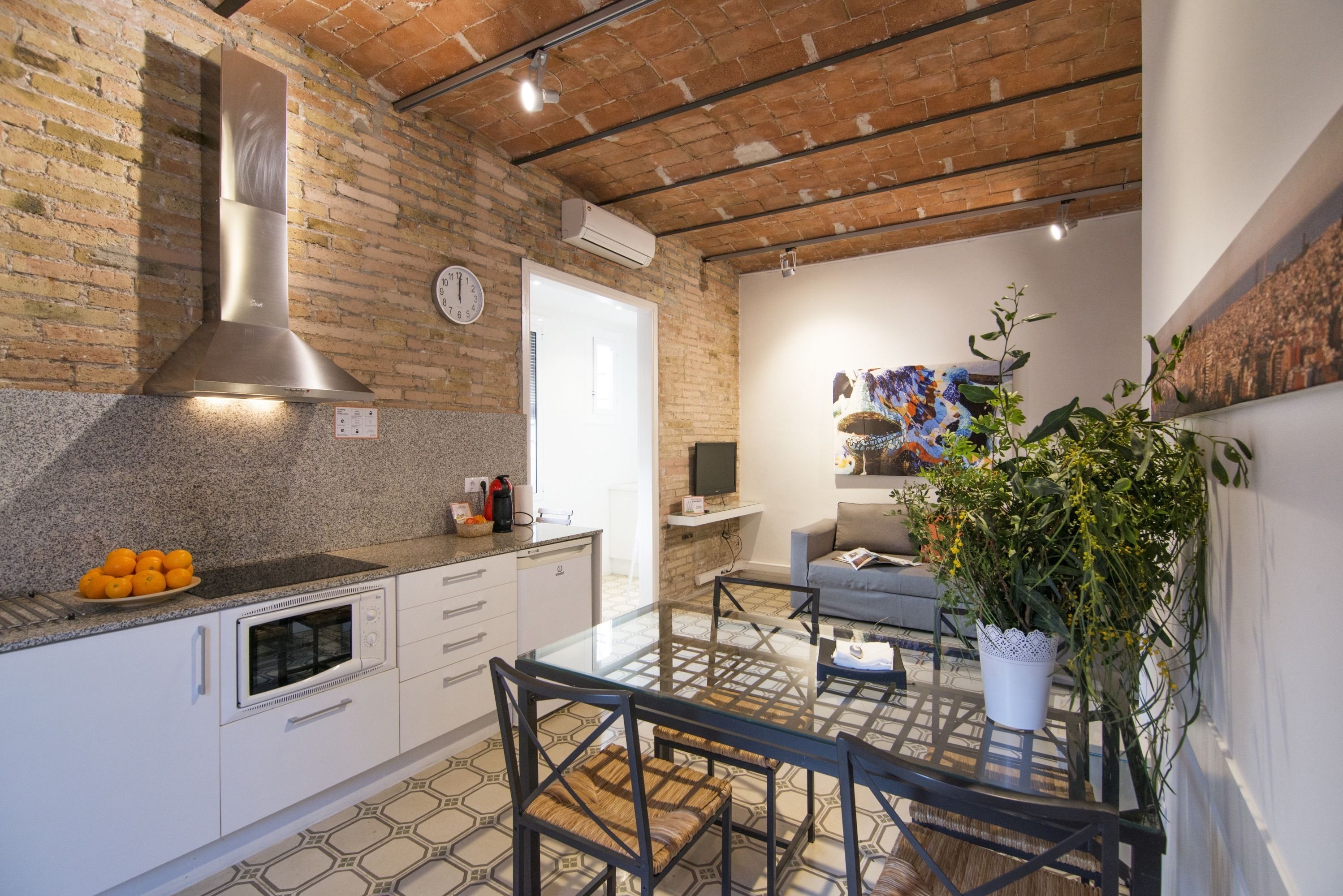 A kitchen with a brick wall, a stainless steel range hood, and a dining area with a glass table and chairs.