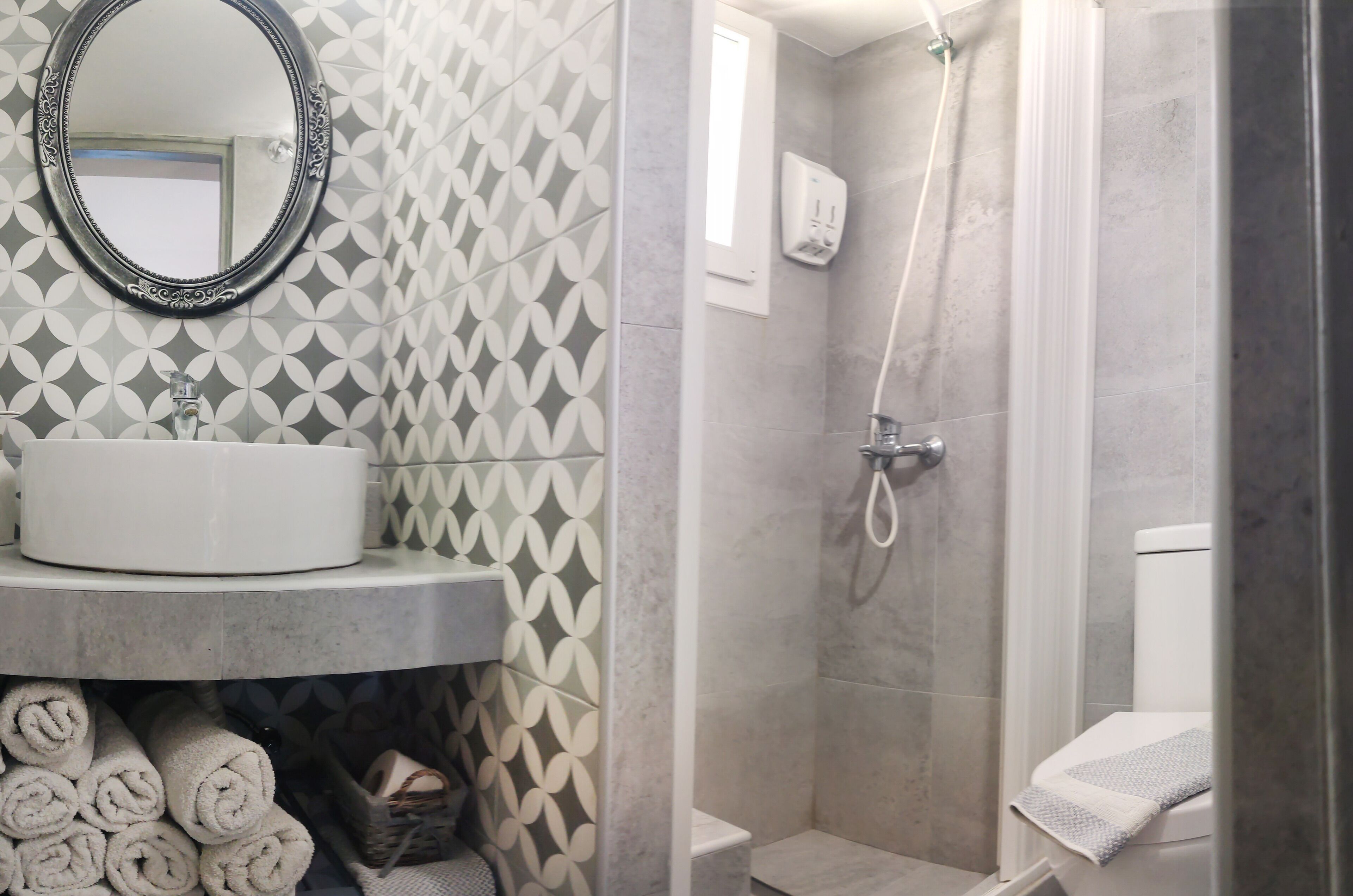 A bathroom with a sink, mirror, towel rolls, shower, and toilet.