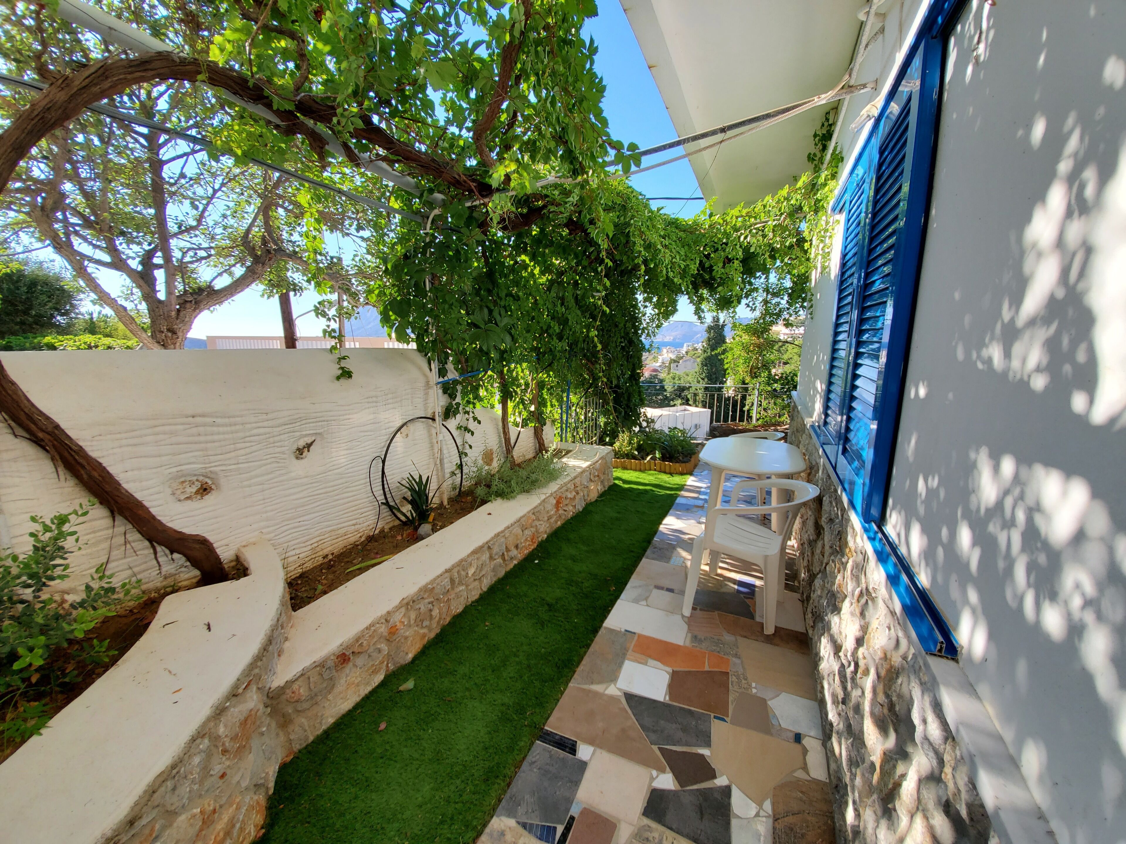 Un patio con un muro de piedra, un pequeño césped y una mesa blanca con sillas.