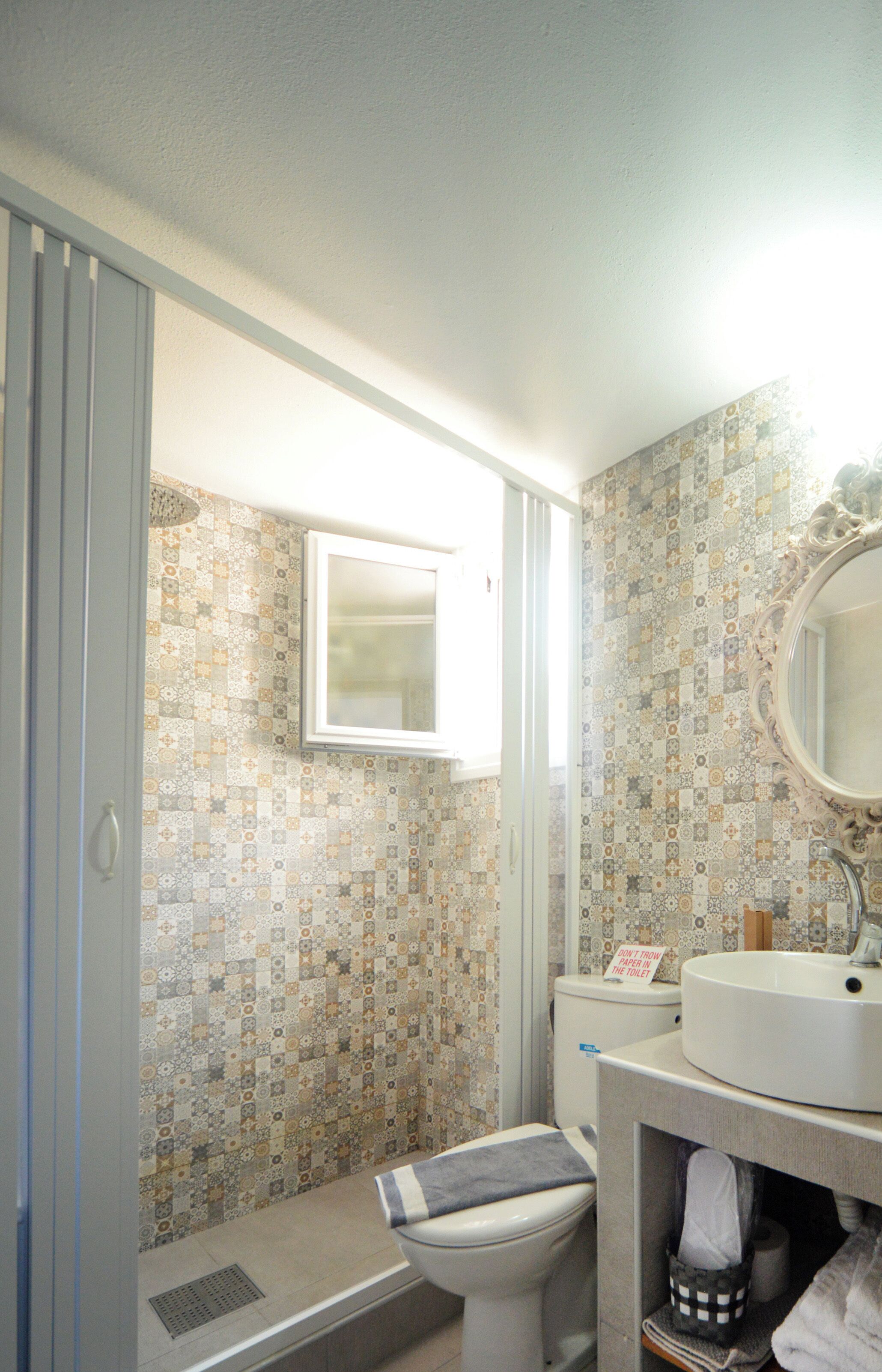 Un baño con baldosas estampadas, un inodoro, un lavamanos y un espejo.