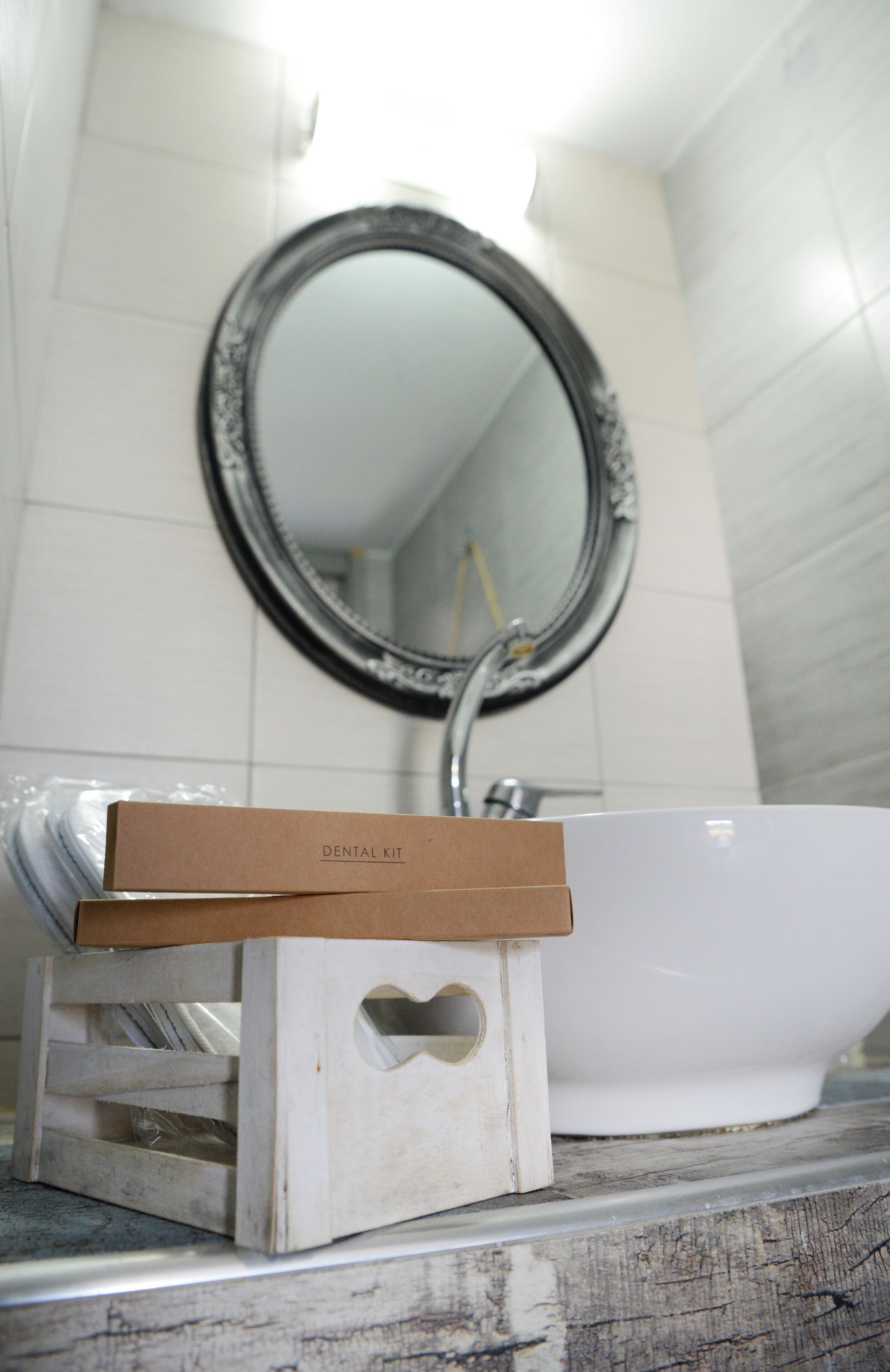 A bathroom with a white sink, a mirror, and a dental kit box on a wooden stand.