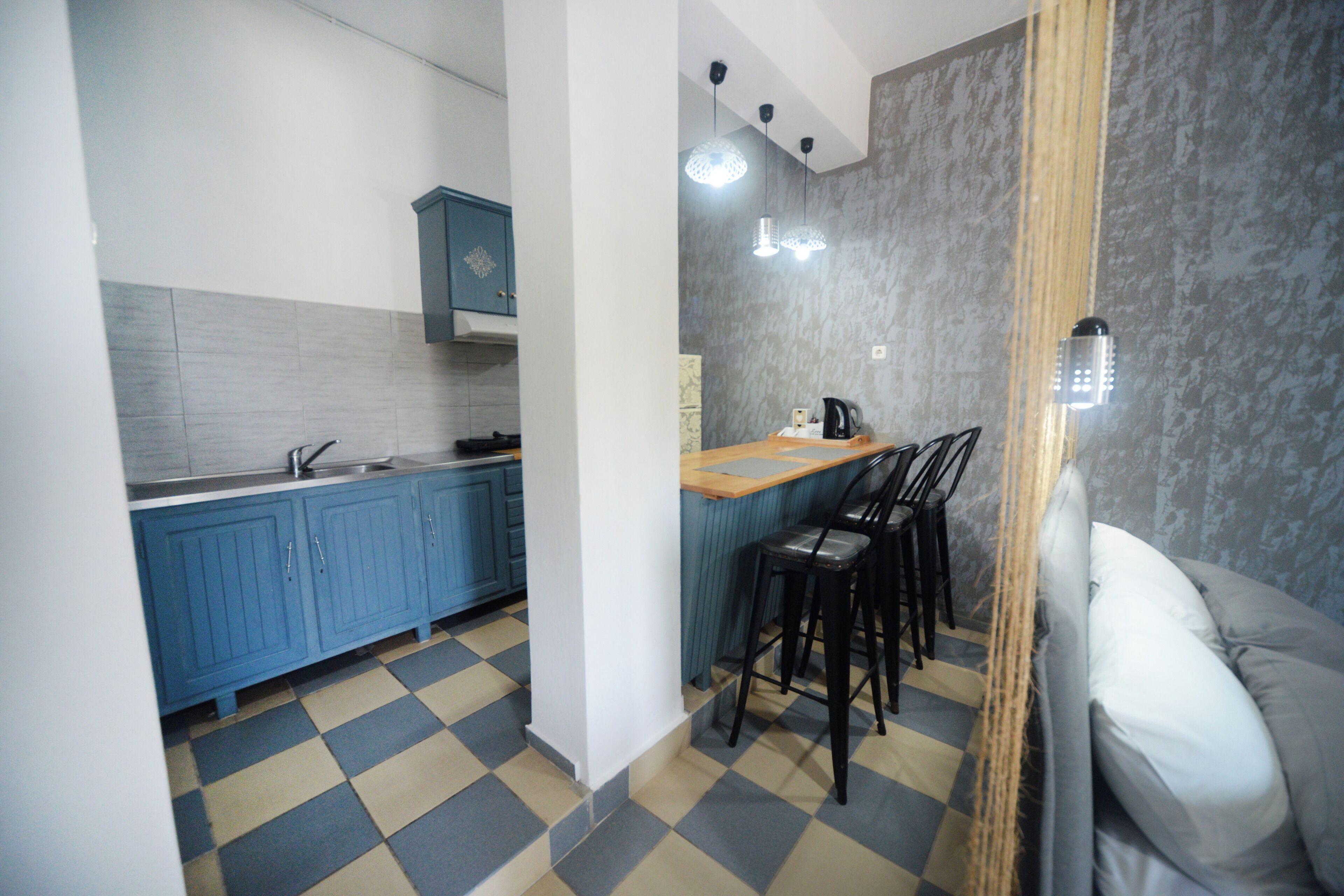 Una cocina compacta con gabinetes azules, piso a cuadros y una zona de bar con taburetes.