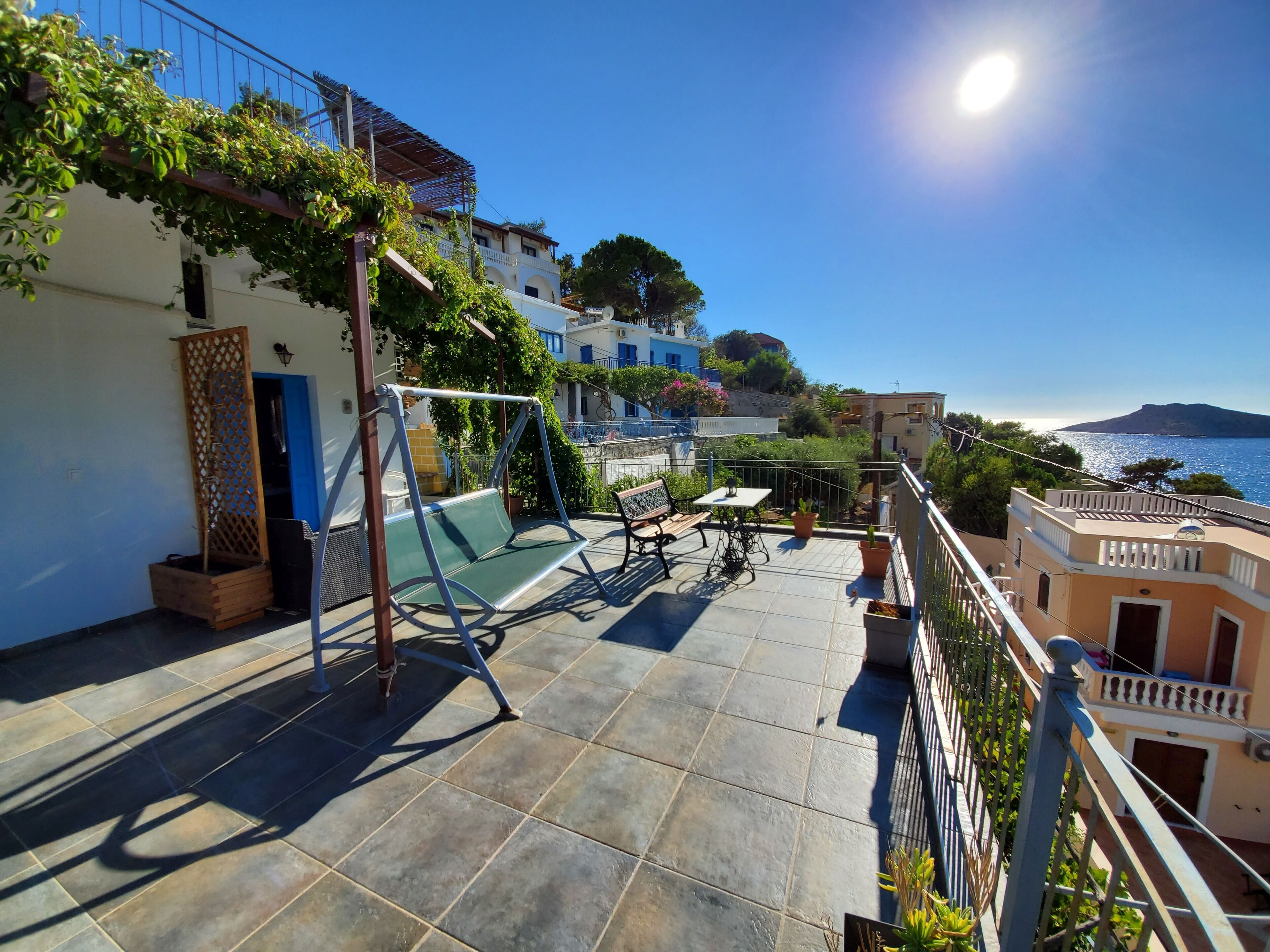 Una terraza con una hamaca, una mesa y sillas, con vistas a la costa, edificios y un cielo despejado.