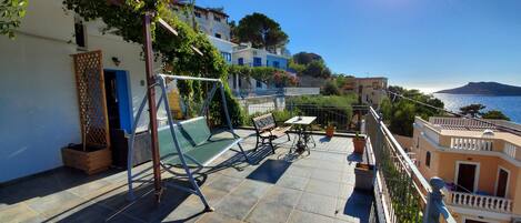 Una terraza con una hamaca, una mesa y sillas, con vistas a la costa, edificios y un cielo despejado.