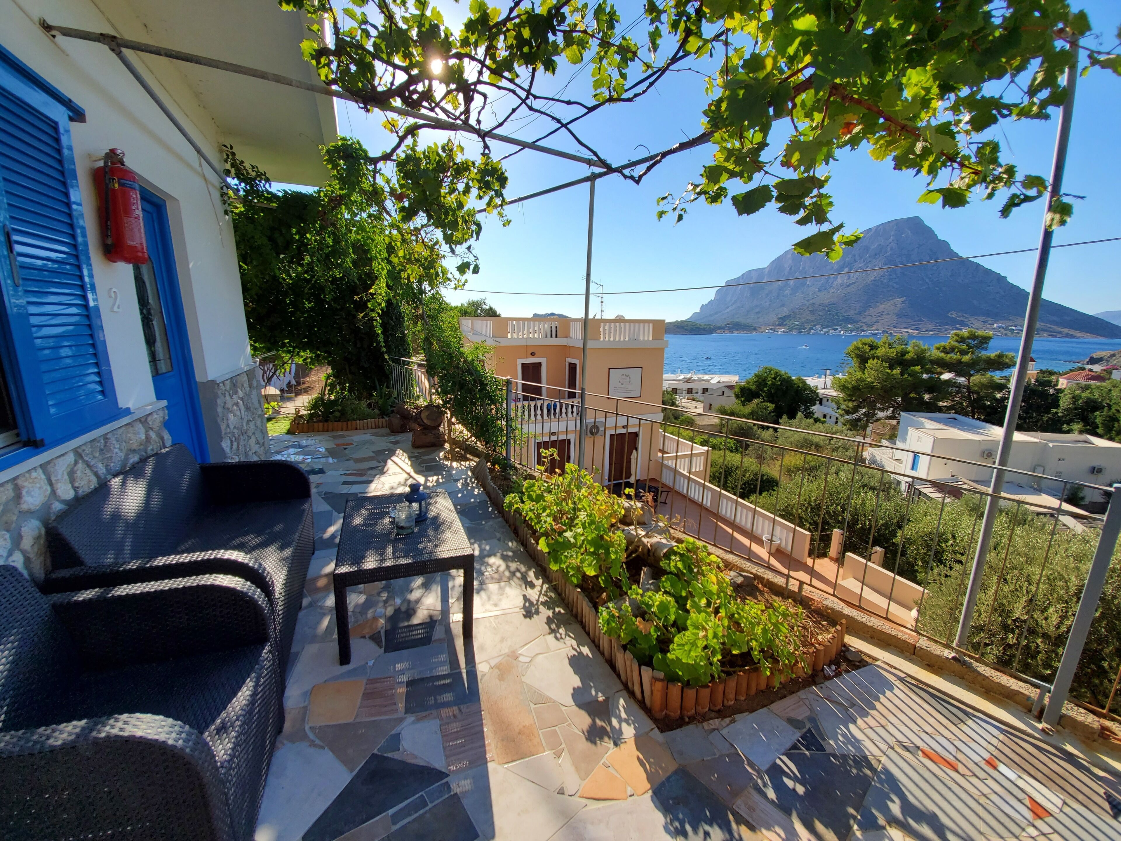 A terrace with a stone floor, outdoor furniture, and a view of the sea and a mountain.