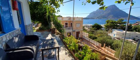 A terrace with a stone floor, outdoor furniture, and a view of the sea and a mountain.