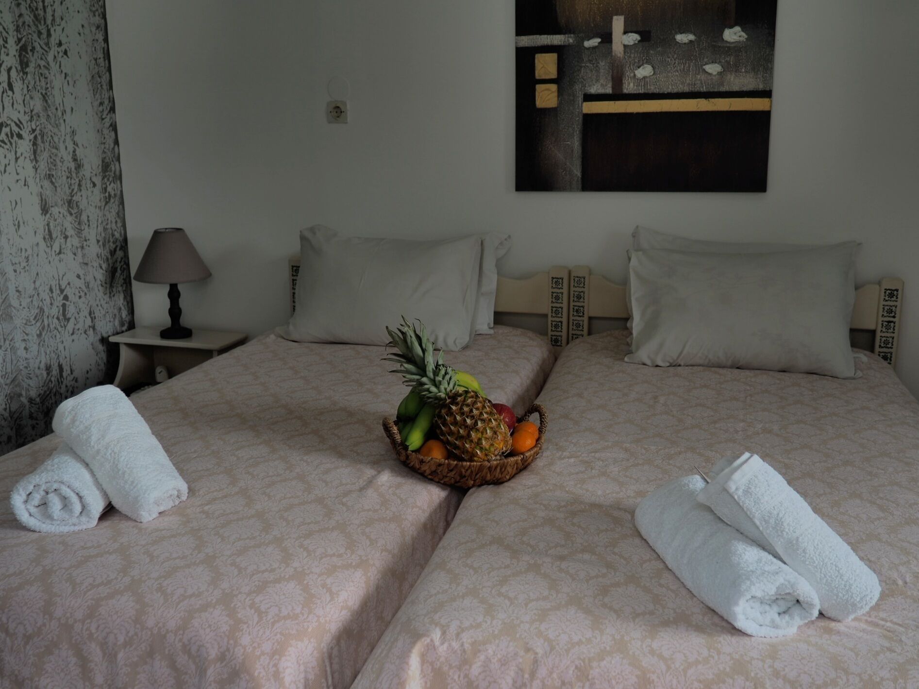 Una camera d'albergo con due letti, un cesto di frutta sul letto a sinistra e asciugamani arrotolati su entrambi i letti.