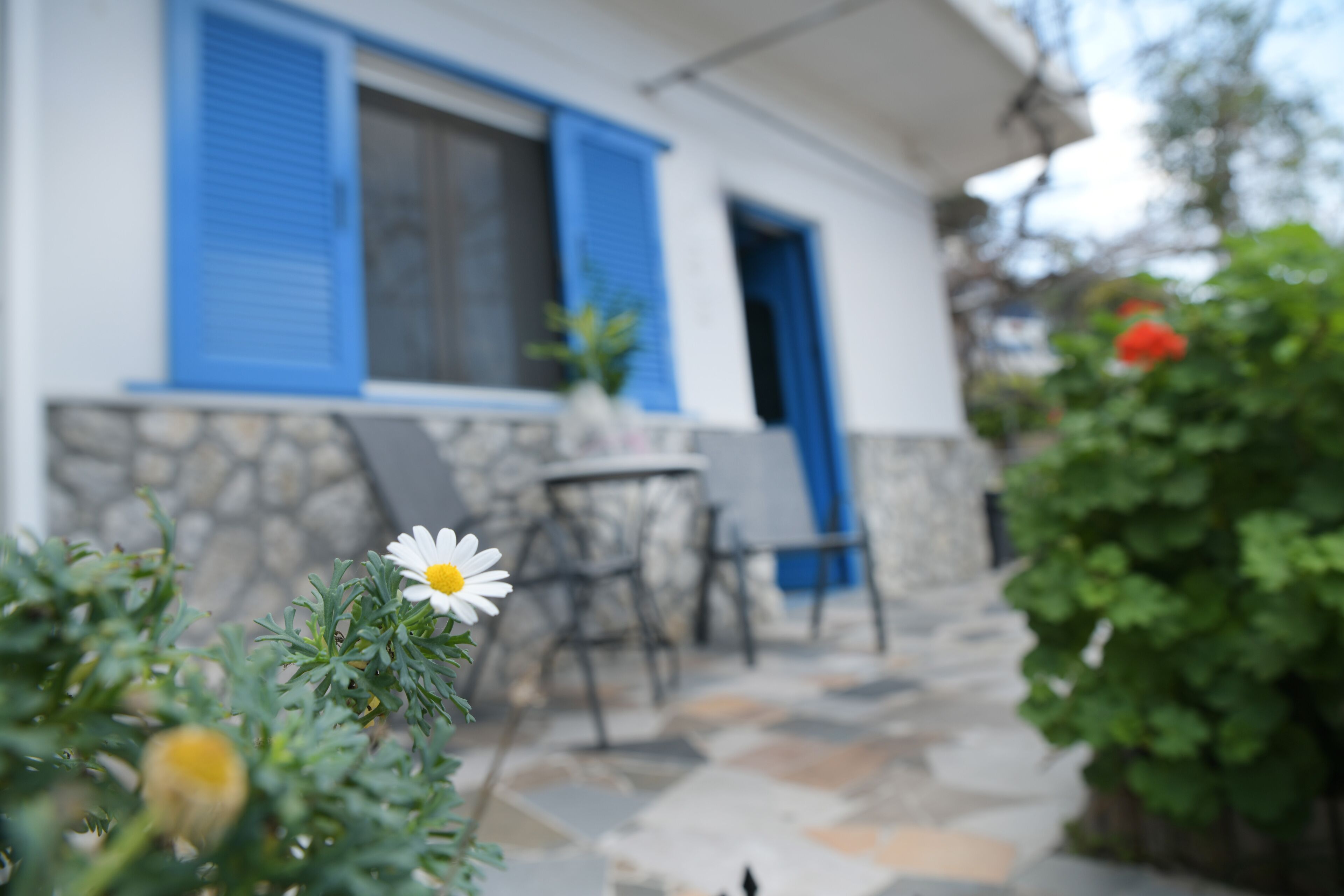 A house with a stone facade, blue shutters, and a small patio with a table and chairs.
