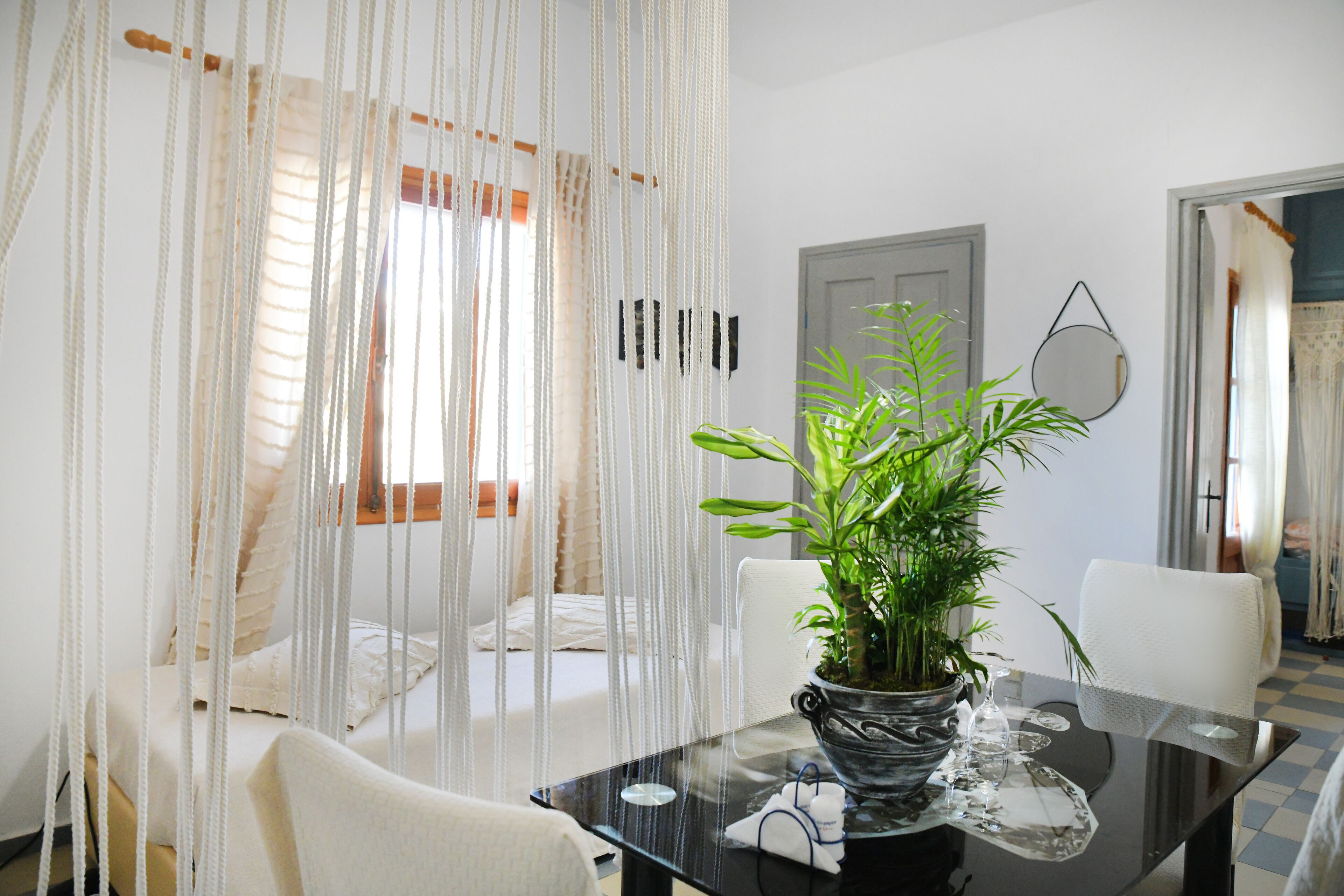 Une pièce comprenant un lit, une table à manger avec des chaises, une plante en pot et un miroir au mur.