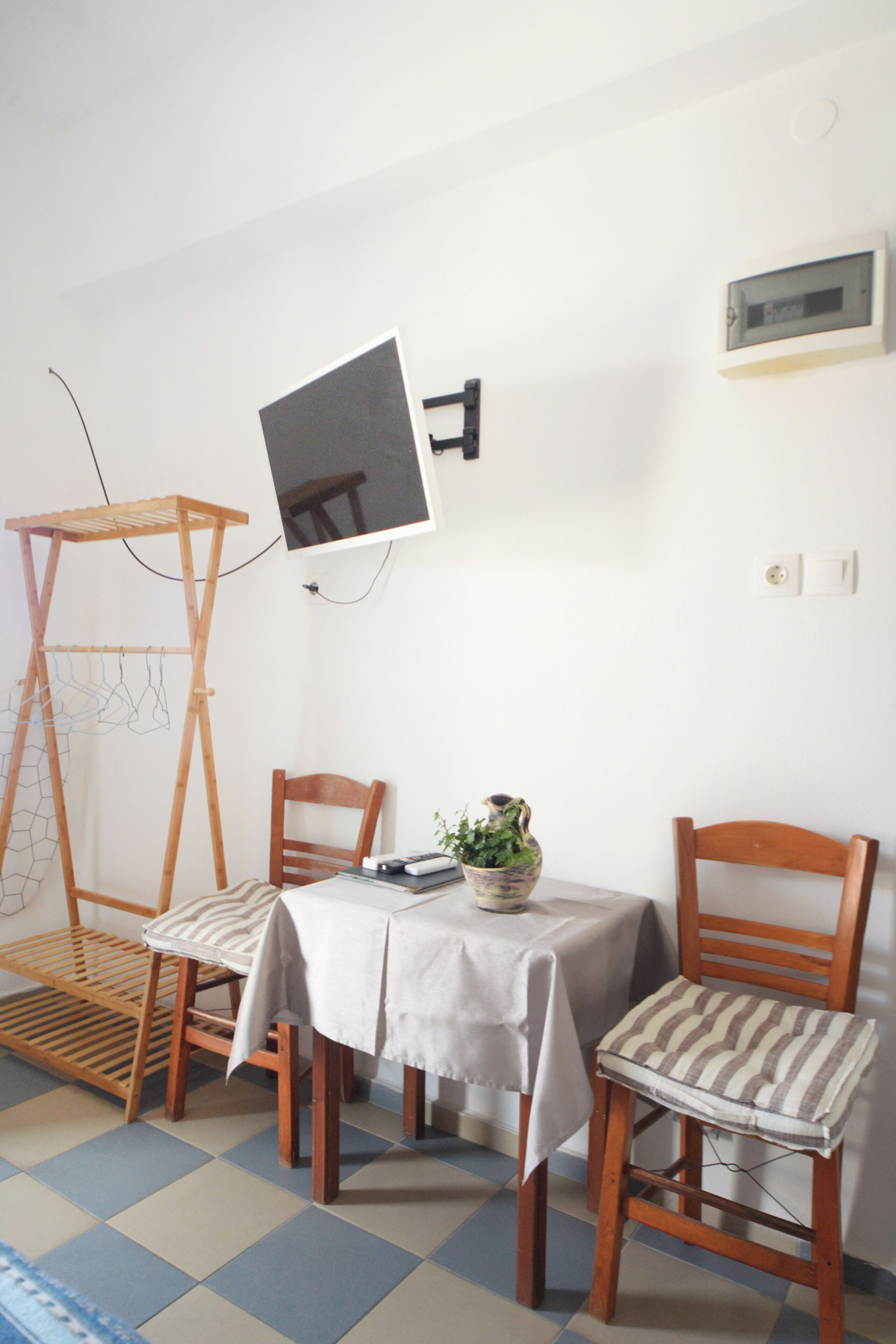 A small dining area with a table, chairs, a hanging clothes rack, and a wall-mounted television.