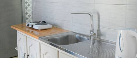 A kitchen with white cabinets, a stainless steel sink, and a white kettle.