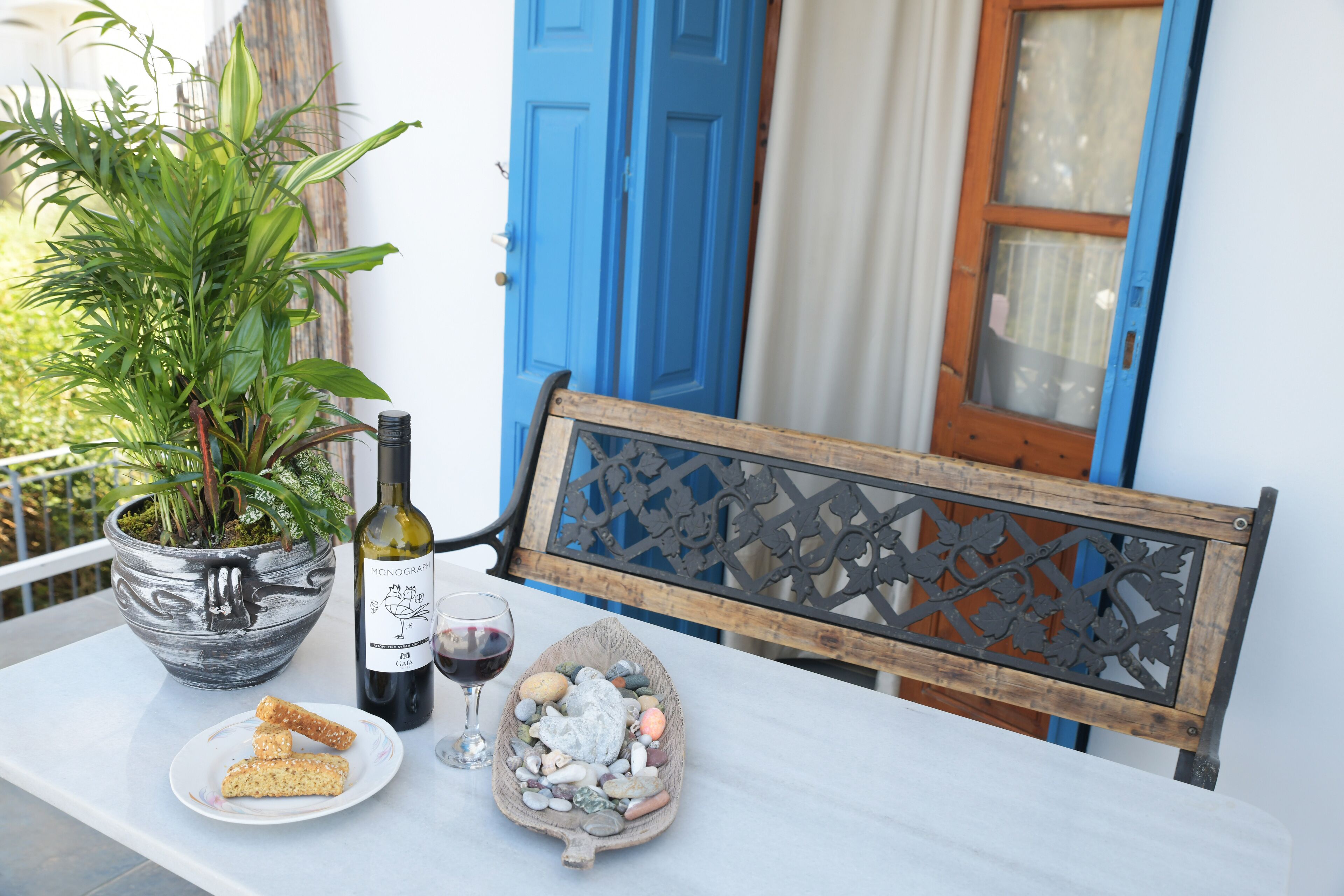 A table with a potted plant, a bottle of wine, a glass of wine, and a bowl of pebbles.