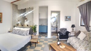 A bedroom with a bed, a sofa, a coffee table, and a view of the bathroom and kitchen. - Panorama Studios & Apartments (Kalymnos)