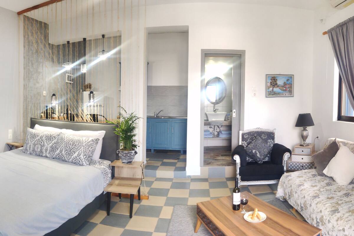 A bedroom with a bed, a sofa, a coffee table, and a view of the bathroom and kitchen.