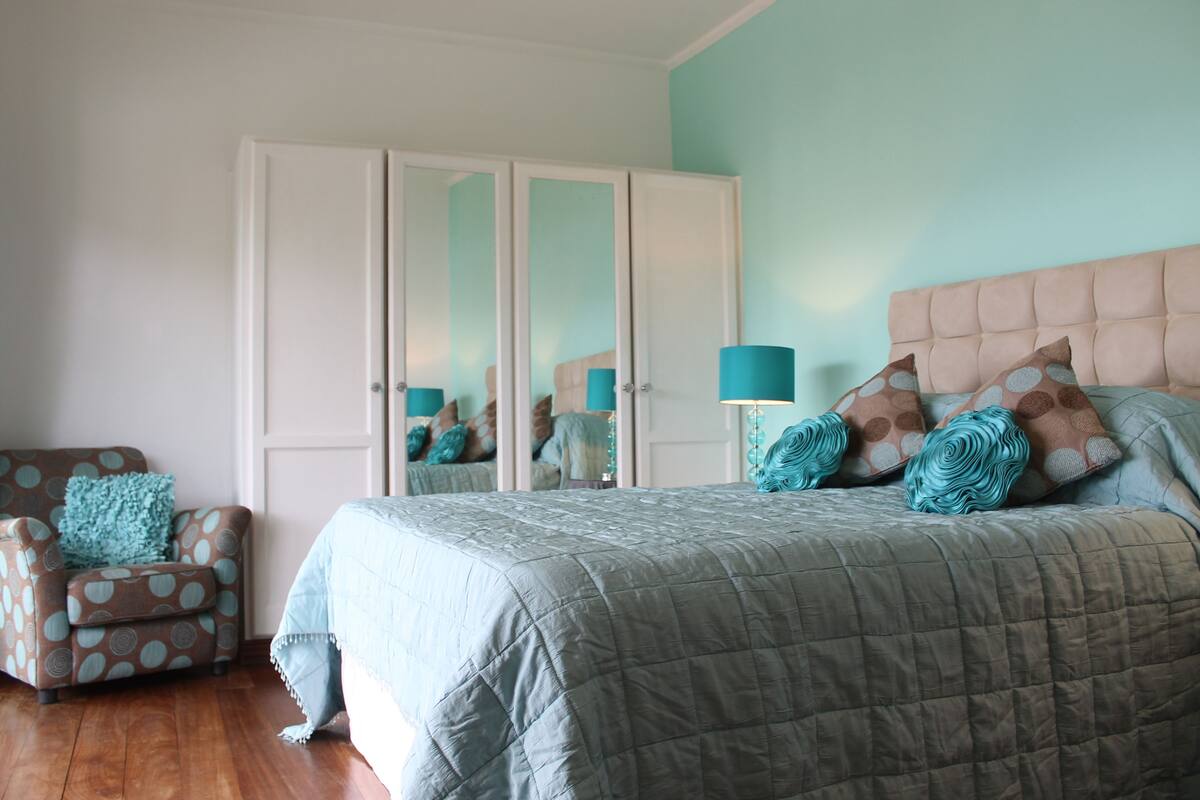 A bedroom with a bed, a chair, a wardrobe, and a mirror.