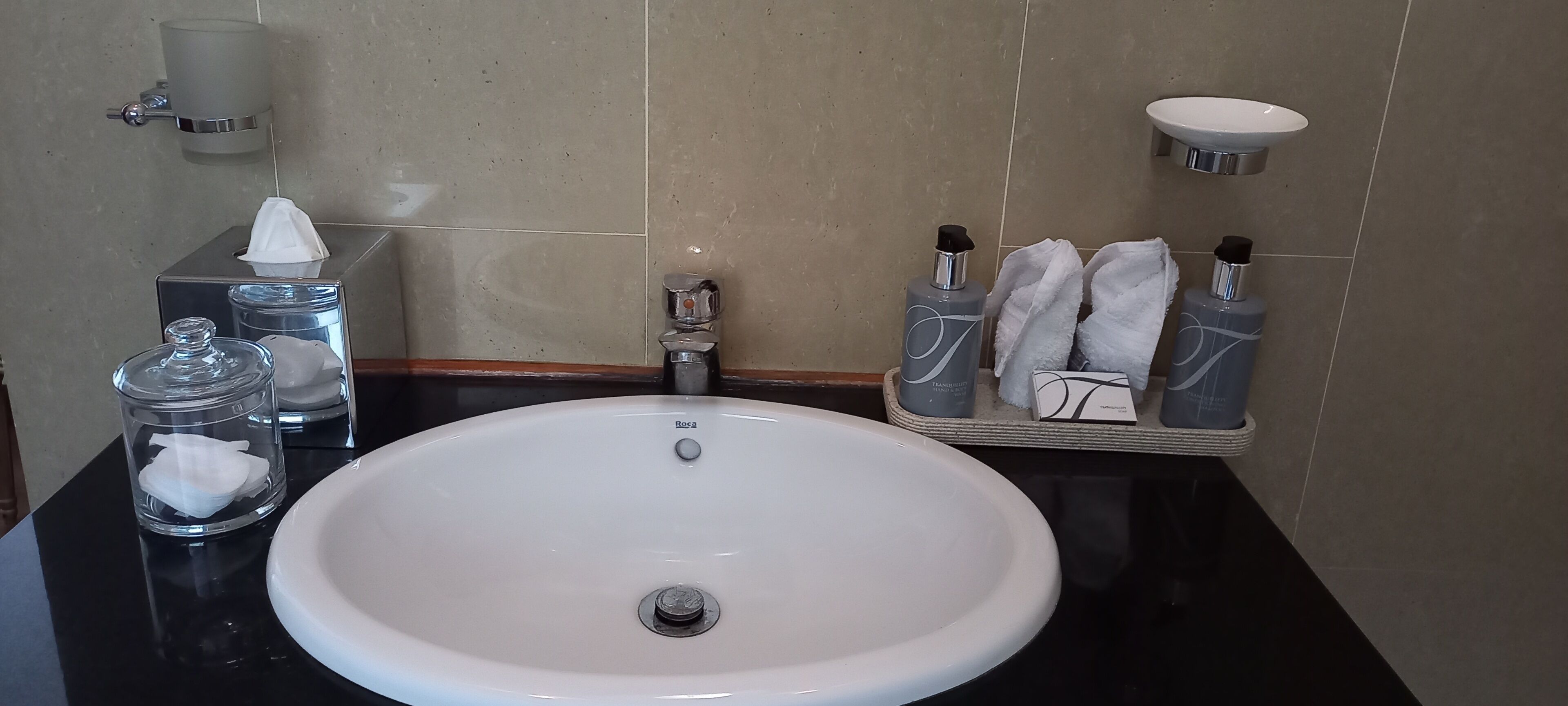 A bathroom with a white sink, a tissue dispenser, a soap dispenser, and a towel rack.