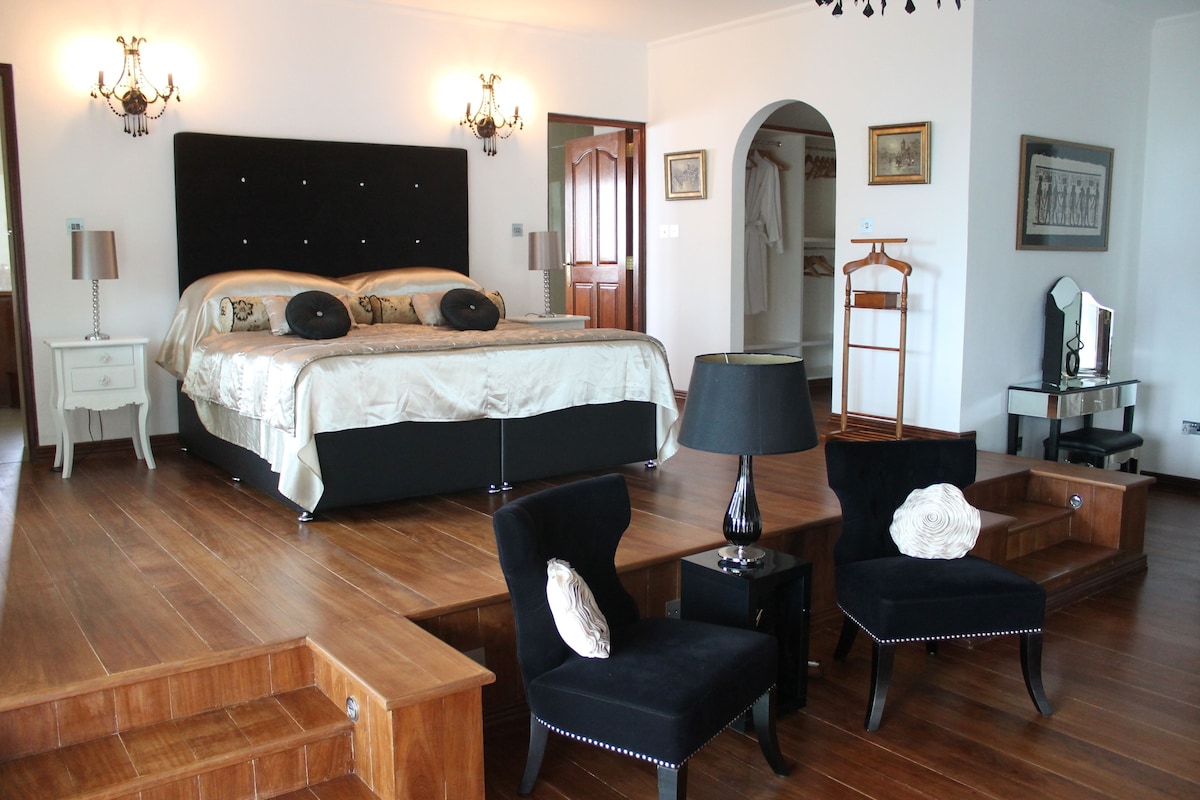Un dormitorio con una cama grande, mesitas de noche, una silla, una lámpara y un espejo.
