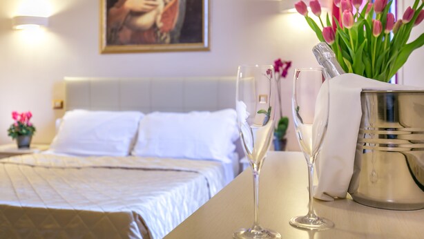 A hotel room with a neatly made bed, a vase with pink tulips, and two champagne flutes on a table. - Monna Clara Affittacamere (Florence)