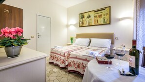 A hotel room with a bed, a bedside table with a bottle of wine, two glasses of wine, a vase with flowers, and a painting on the wall. - Monna Clara Affittacamere (Florence)