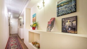 A hallway with a patterned carpet, a potted plant, and wall-mounted decor including framed pictures and magazines. - Monna Clara Affittacamere (Florence)