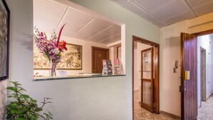 A reception area with a glass counter, a framed painting, a potted plant, and a wooden door. - Monna Clara Affittacamere (Florence)