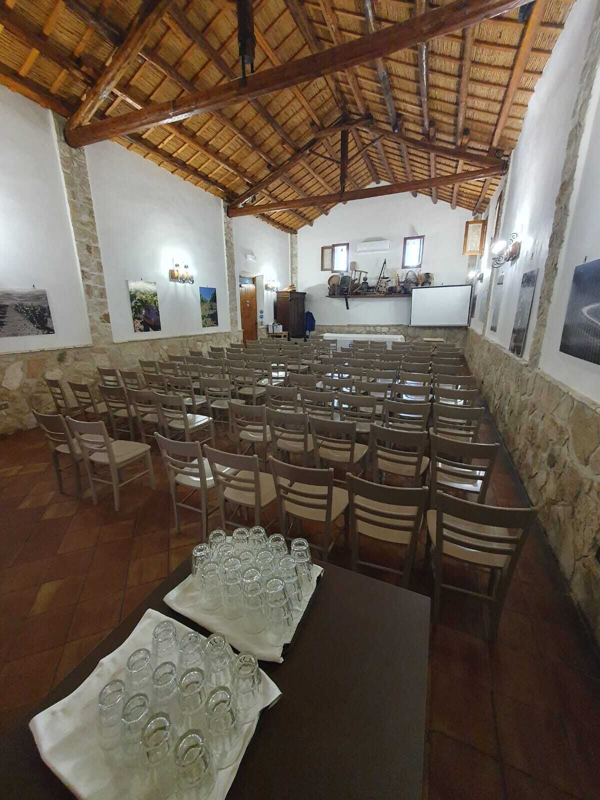 A room with a high wooden ceiling and stone walls, arranged with rows of chairs and tables, some with glasses on them.