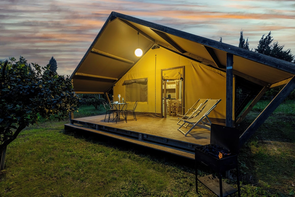 A geodesic dome tent with a wooden deck, a grill, and a table with chairs.