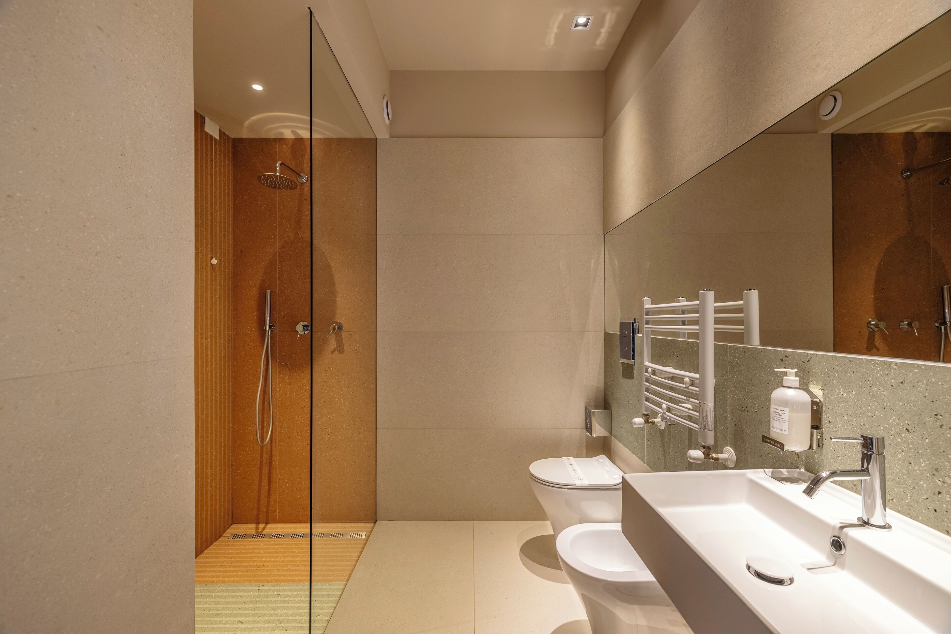 A modern bathroom with a glass-enclosed shower, a large mirror, and a white sink with a soap dispenser.