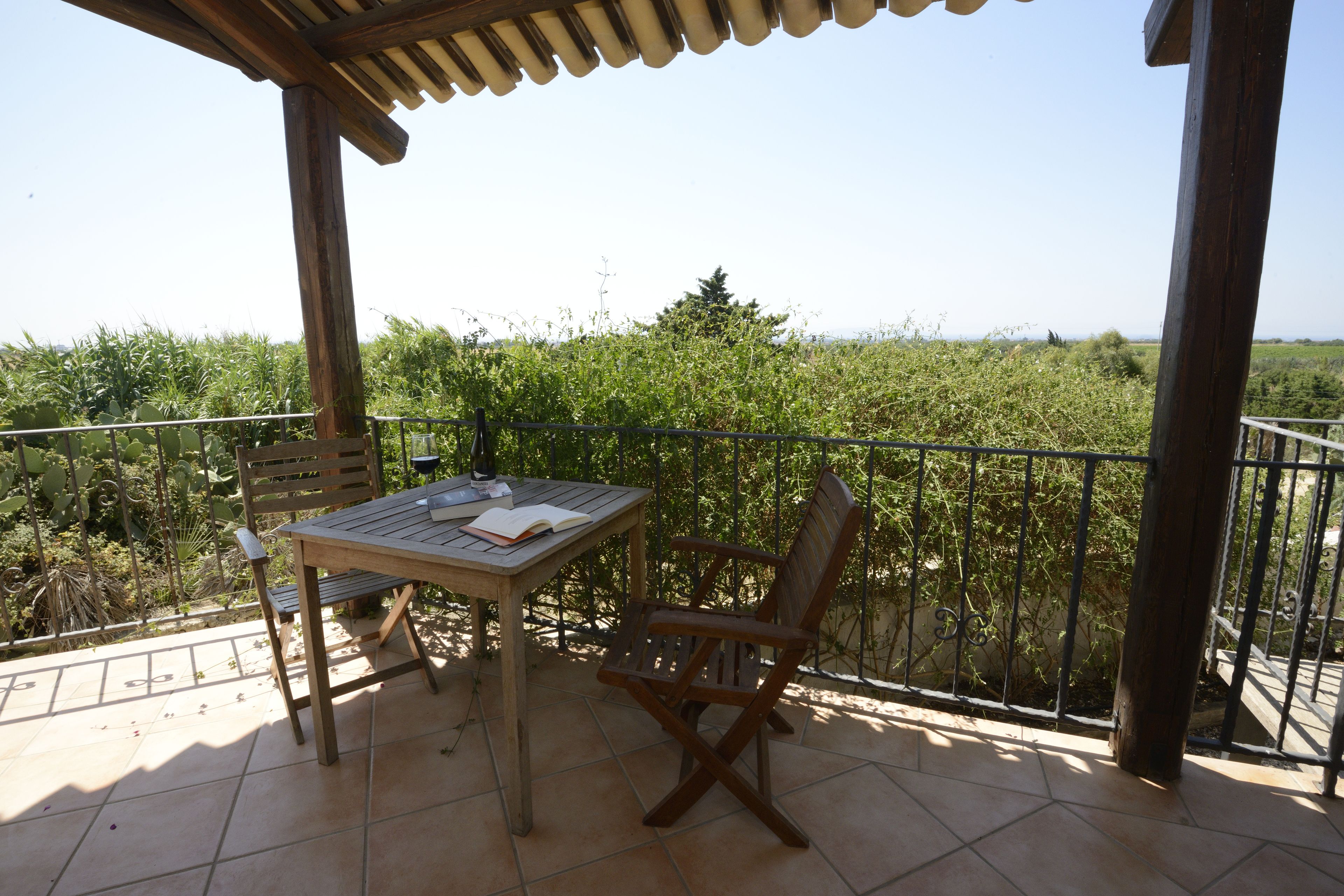 A wooden table and chair set on a balcony with a view of greenery and a clear sky.