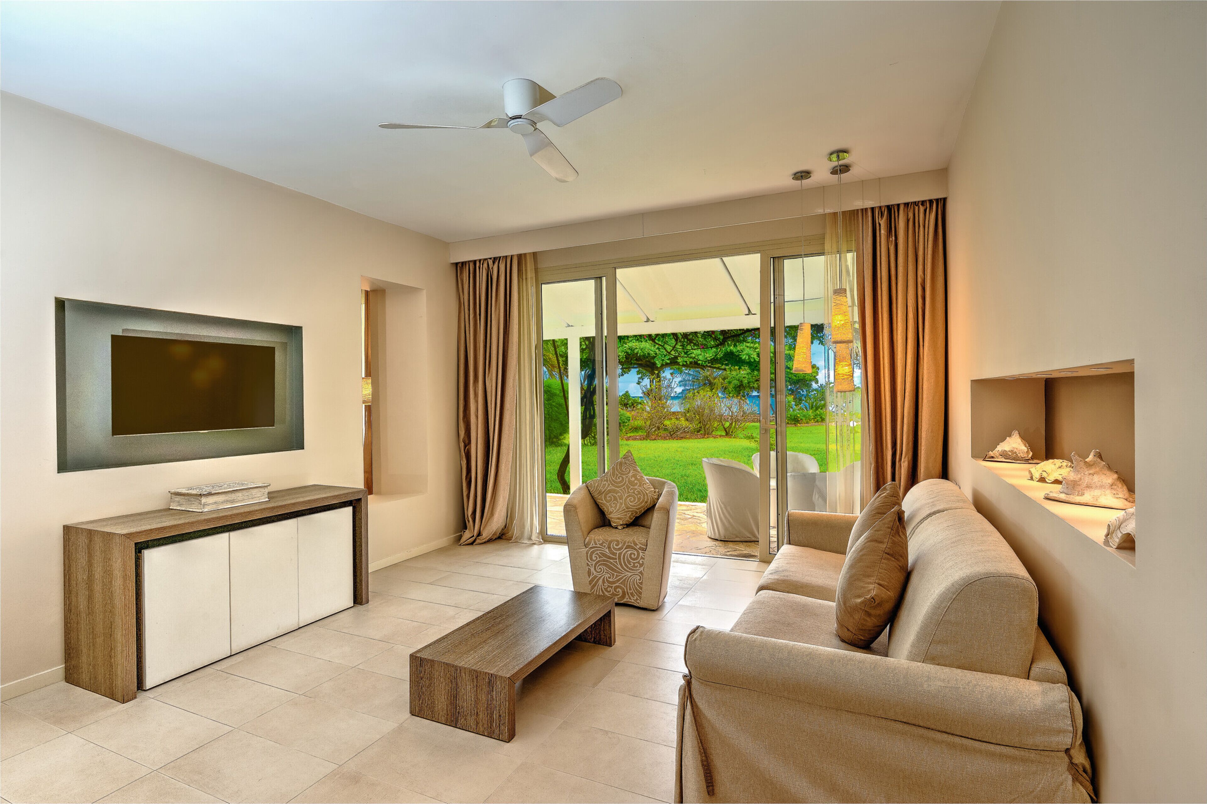 Una sala de estar moderna con un televisor de pantalla plana, una mesa de centro de madera, un sofá color beige y un sillón estampado.