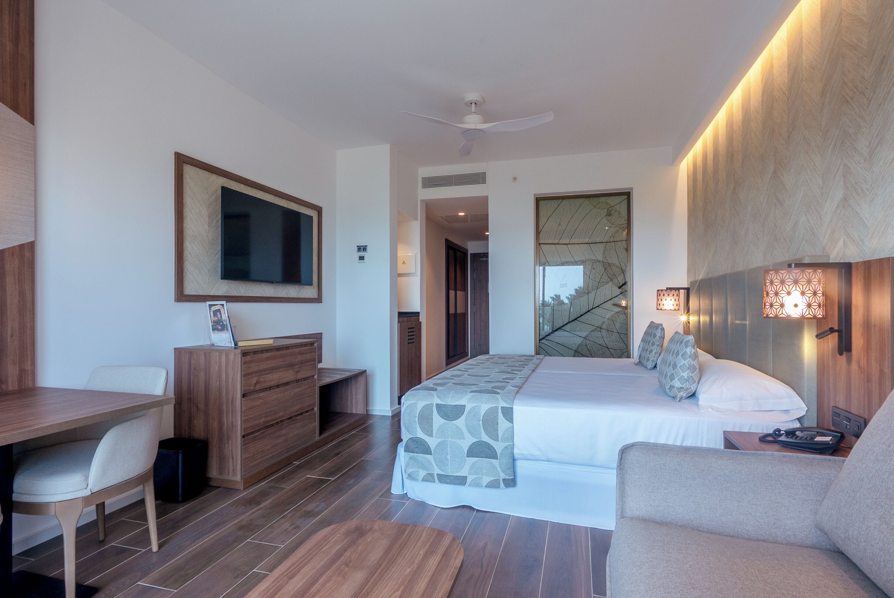 Una habitación de hotel moderna con una cama grande, un escritorio, una silla, un armario y un televisor.