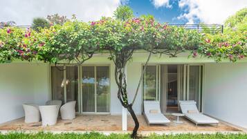 A modern outdoor lounge area with a glass-enclosed patio, white lounge chairs, and a small tree with pink flowers.