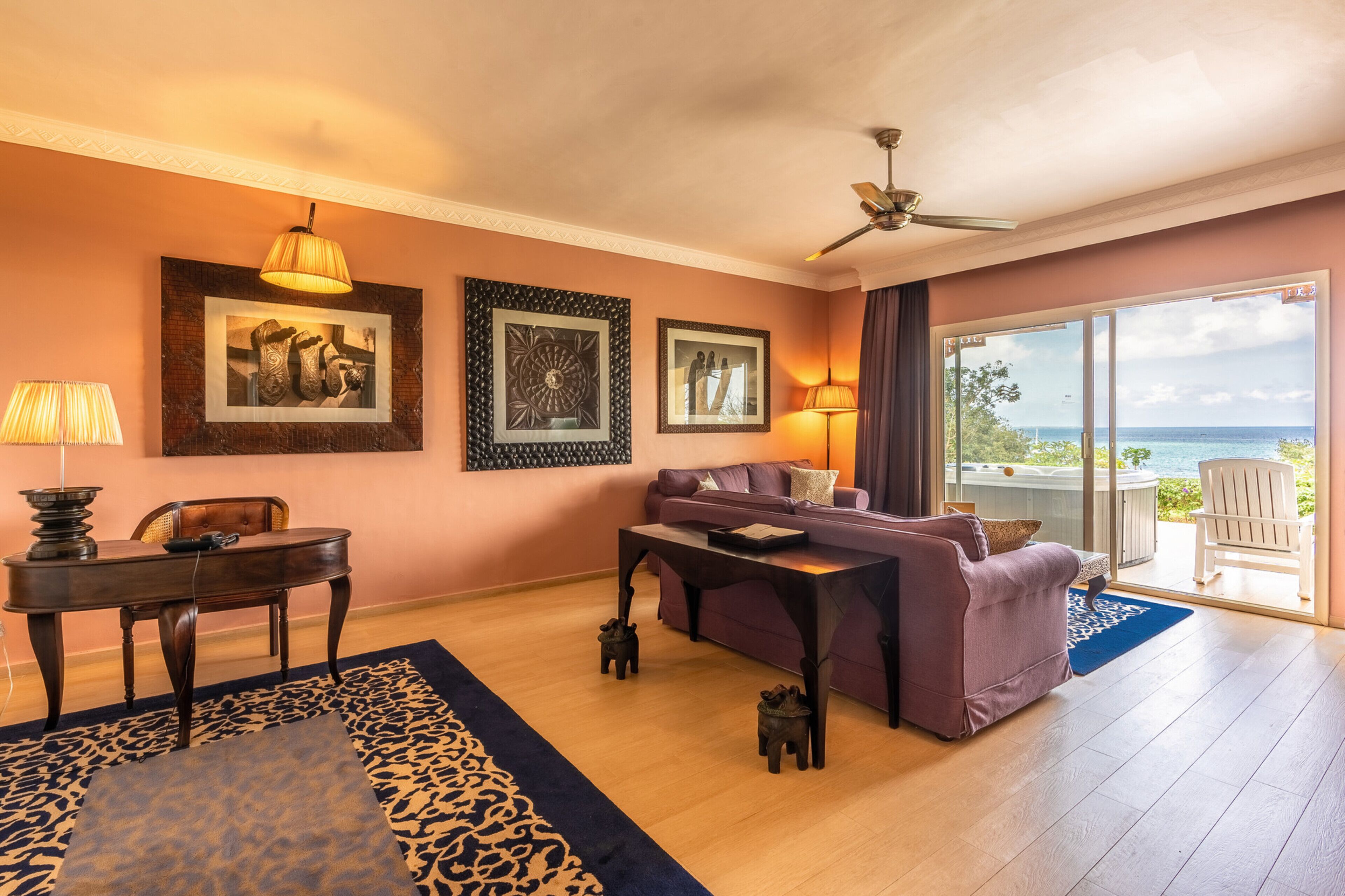 A living room with a purple sofa, a wooden table, and a view of the ocean through a sliding glass door.