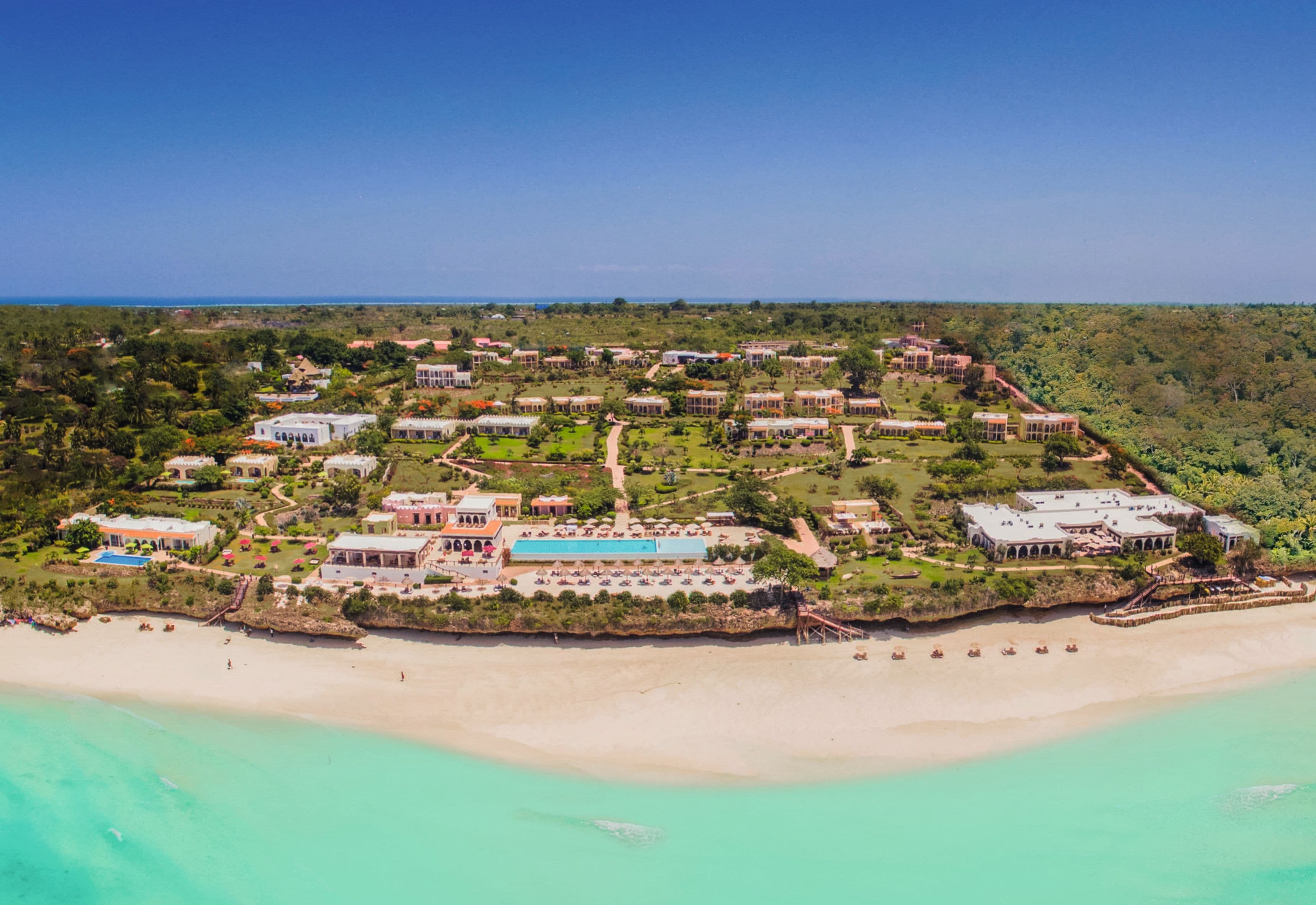 An aerial view of a resort with multiple buildings, a beach, and clear turquoise waters.