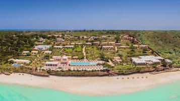 An aerial view of a resort with multiple buildings, a beach, and clear turquoise waters.
