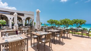 An outdoor dining area with tables and chairs, umbrellas, and a view of the ocean. - Hotel Riu Palace Zanzibar - All Inclusive (Nungwi)